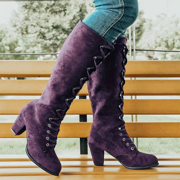 Paarse suède laarzen met hoge hak en veters, gedragen door persoon in blauwe jeans op houten bank. Stijlvolle damesmode, herfst/winter schoenen.