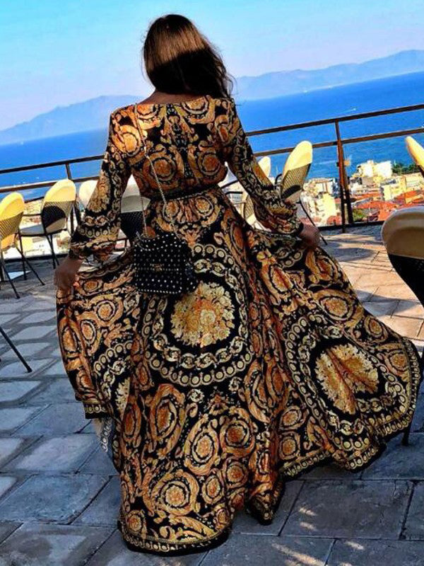 Vrouw in kleurrijke, lange jurk met barokprint op balkon met zeezicht; modieuze outfit, zomerjurk, vakantie, elegantie, modeaccessoires.
