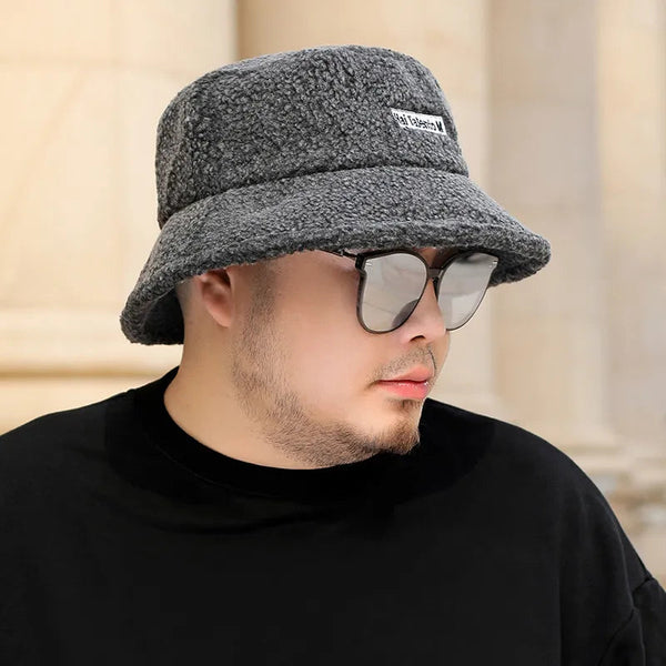 Grijze bucket hat van fleece met label, gedragen door man met zonnebril. Stijlvolle hoed voor herenmode, ideaal voor casual winterlooks.