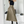Vrouw in zwarte mouwloze top en olijfgroene midi-rok met riem, poseert voor spiegel. Modieuze outfit, hoge laarzen, moderne kledingstijl.
