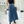 Vrouw in zwarte top en blauwe midi-rok met riem, poseert voor spiegel. Stijlvolle outfit, modeaccessoires op achtergrond, moderne winkelomgeving.