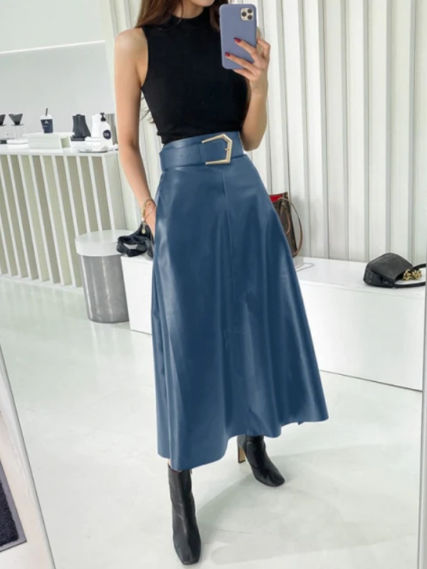 Vrouw in zwarte top en blauwe midi-rok met riem, poseert voor spiegel. Stijlvolle outfit, modeaccessoires op achtergrond, moderne winkelomgeving.