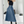 Vrouw in zwarte top en blauwe leren rok met riem, poseert voor spiegel. Modieuze outfit, hoge hakken, moderne stijl, minimalistisch interieur.