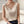 Vrouw in elegante witte satijnen top met V-hals, zittend op een bank. Modieuze dameskleding, minimalistisch ontwerp, casual chique stijl.