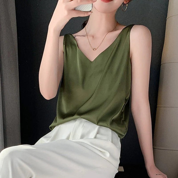 Vrouw in olijfgroene satijnen top en witte broek, modieuze zomerkleding, elegante damesmode, minimalistische stijl, trendy outfit.