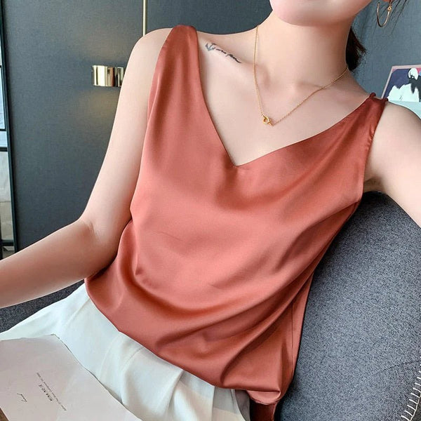 Vrouw in satijnen top met V-hals, roestkleurig, zittend op een stoel. Elegante damesmode, trendy zomeroutfit, minimalistische stijl.