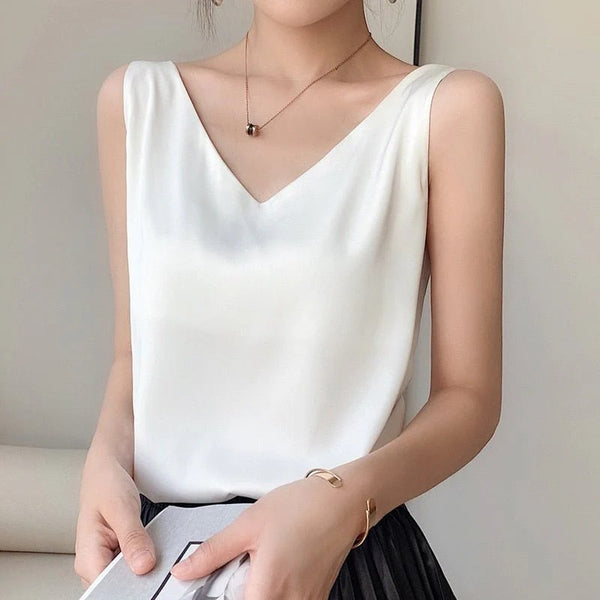 Vrouw in witte mouwloze top met V-hals, zwarte geplooide rok, minimalistische ketting en armband. Elegante zomermode, casual chique stijl.