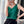 Vrouw in groene mouwloze top en zwarte rok, zittend bij raam met smartphone. Stijlvolle zomermode, casual outfit, moderne sieraden.