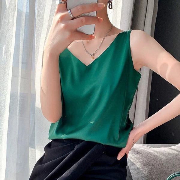 Vrouw in groene mouwloze top en zwarte rok, zittend bij raam met smartphone. Stijlvolle zomermode, casual outfit, moderne sieraden.