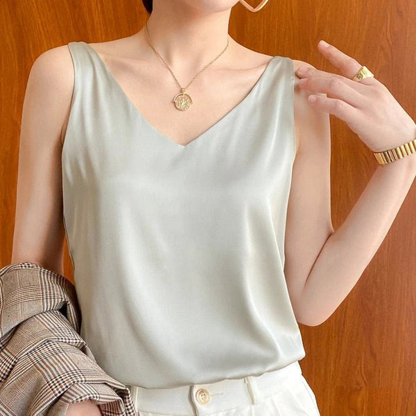 Vrouw in zijden top met V-hals, gouden ketting en horloge, poseert voor houten achtergrond. Elegante mode, minimalistische stijl, dameskleding.
