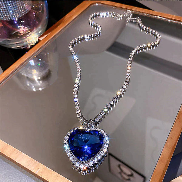 Hartvormige blauwe saffieren hanger met diamanten ketting op spiegelend oppervlak, luxe sieraden, elegante halsketting, glinsterende edelstenen.