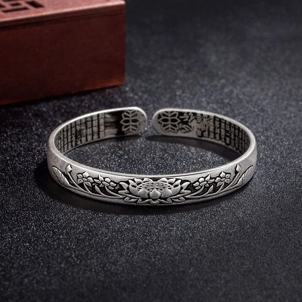 Zilveren armband met lotusgravure, open ontwerp, op donkere achtergrond. Handgemaakt sieraad, bohemian stijl, ideaal voor damesmode en accessoires.