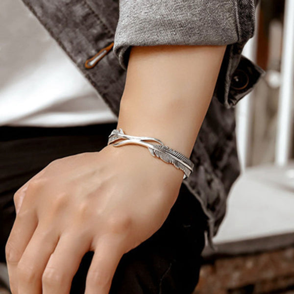 Zilveren armband met veerontwerp om pols van persoon in casual kleding. Modieuze sieradenaccessoire, stijlvol en elegant.