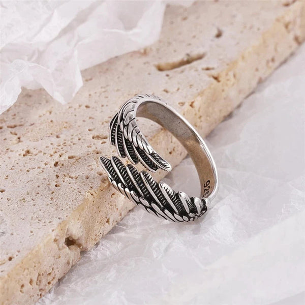 Zilveren ring met verenontwerp op beige achtergrond, sieradenaccessoire, modieuze damesring, handgemaakt, elegant en stijlvol.