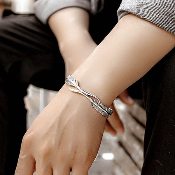 Zilveren armband met veerontwerp om pols van persoon, stijlvolle sieradenaccessoire, modieuze unisex armband, elegant en modern design.