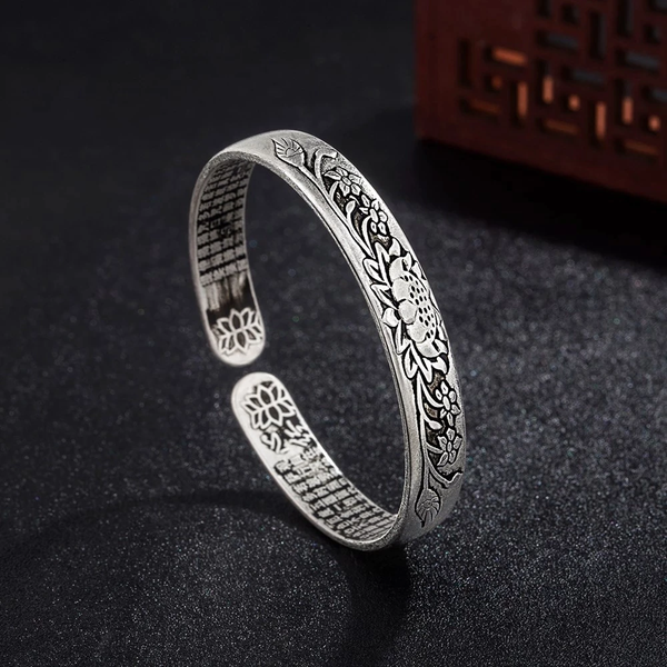 Zilveren armband met bloemenpatroon, open ontwerp, op zwarte achtergrond. Elegante sieraden, handgemaakt, vintage stijl, cadeau-idee.