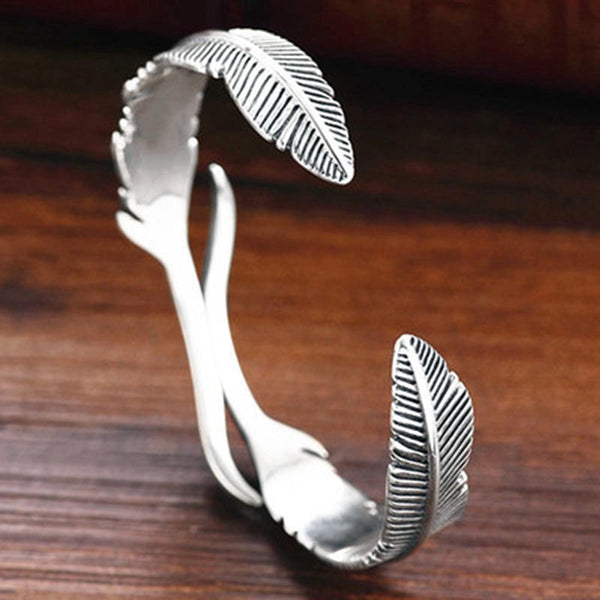 Zilveren armband met veerontwerp op houten achtergrond, sieradenaccessoire, modieuze damesarmband, elegant en stijlvol.