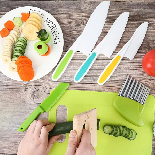 Drie gekartelde kindermessen met kleurrijke handvatten op houten tafel, naast gesneden groenten en een snijplank. Veilig keukenhulpmiddel voor kinderen.