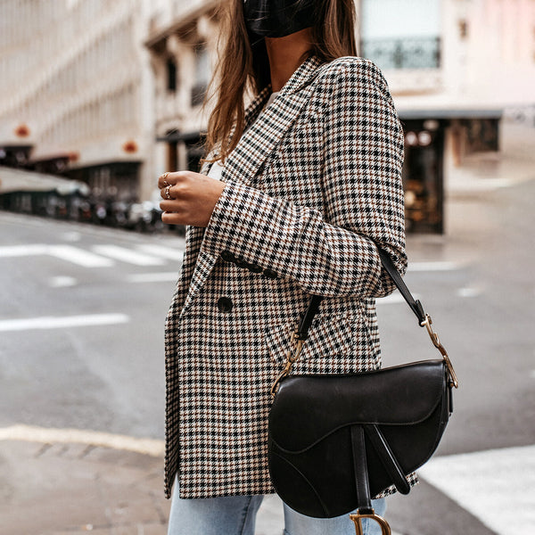 Vrouw met geruite blazer en zwarte schoudertas op straat. Modieuze herfstoutfit, casual stijl, stedelijke achtergrond.
