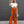 Vrouw in trendy outfit met witte gebreide crop top en oranje flared broek, draagt zonnebril en beige tas, poseert voor grijze achtergrond.