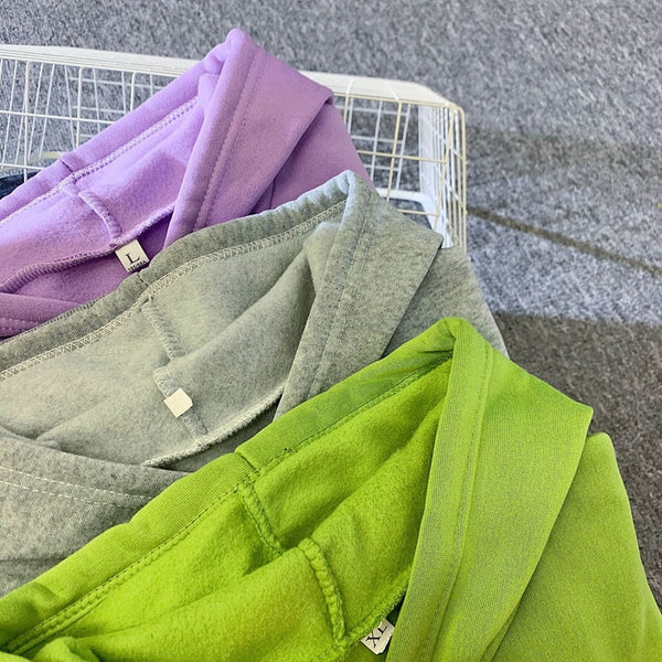 Drie kleurrijke hoodies in een wasmand: paars, grijs en groen. Comfortabele katoenen truien, perfect voor casual mode en streetwear trends.