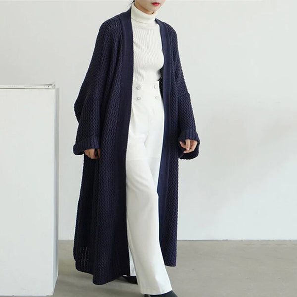 Vrouw in lange, donkerblauwe gebreide cardigan, witte coltrui en witte broek. Stijlvolle herfstmode, minimalistisch design, casual chic outfit.