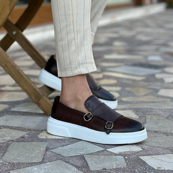 Bruine heren gevulkaniseerde schoenen met dubbele gesp, zwart slip-on design, handgemaakt, gedragen door model op stenen vloer.