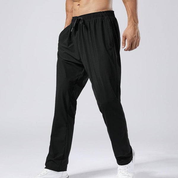 Man in zwarte sportbroek en witte sneakers, staand tegen een neutrale achtergrond. Comfortabele trainingsbroek voor heren, ideaal voor fitness en casual gebruik.
