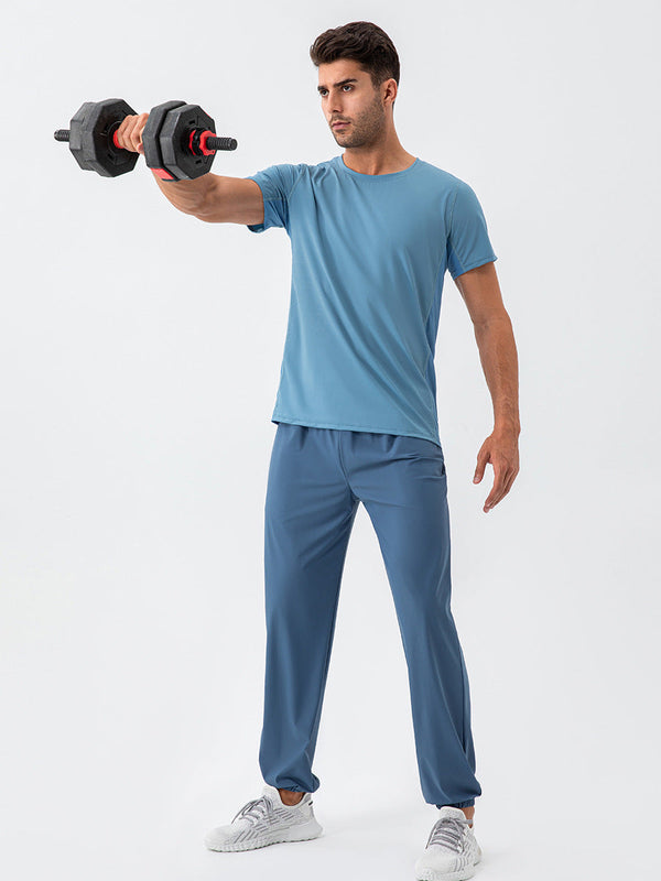 Man in blauwe sportkleding tilt een zwarte halter omhoog tegen een witte achtergrond. Fitness, krachttraining, sportkleding, workout.