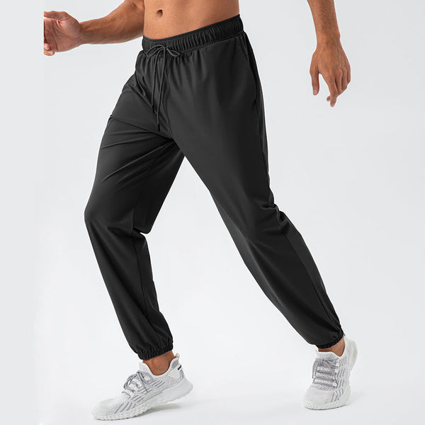 Man in zwarte sportbroek en grijze sneakers, wandelend op witte achtergrond. Comfortabele trainingsbroek, ideaal voor fitness en casual gebruik.