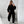 Vrouw in zwarte oversized trui en broek poseert voor spiegel, houdt smartphone vast. Modieuze casual outfit, trendy sneakers, minimalistisch interieur.