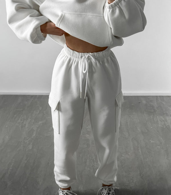 Vrouw in witte joggingbroek en hoodie, casual sportkleding, comfortabele loungewear, trendy mode, minimalistisch design, grijze vloer.