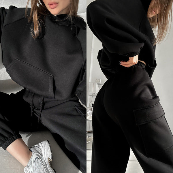 Vrouw in zwarte oversized hoodie en joggingbroek, modieuze streetwear, comfortabele casual outfit, witte sneakers, minimalistisch interieur.