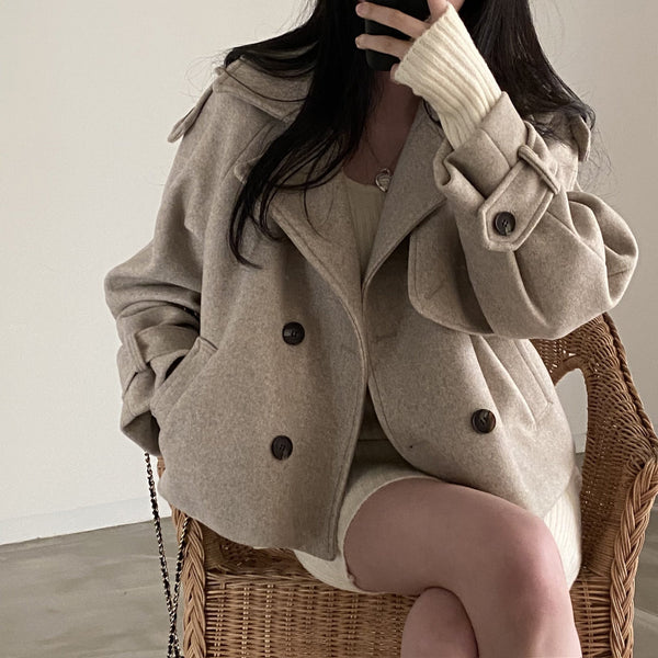 Vrouw in beige wollen jas en gebreide jurk, zittend op rieten stoel, minimalistische mode, herfst winter outfit, stijlvolle dameskleding.