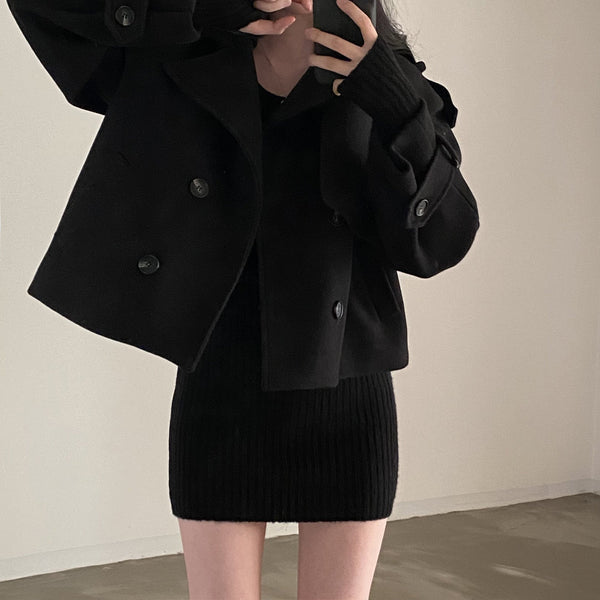 Vrouw in zwarte wollen jas en geribde jurk maakt selfie in minimalistische kamer. Modieuze winterkleding, trendy damesmode, casual stijl.