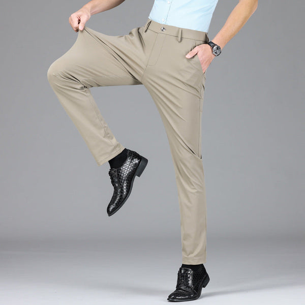 Man in beige stretchbroek, witte blouse en zwarte leren schoenen, toont flexibiliteit van de broek. Comfortabele herenmode, stijlvolle zakelijke outfit.