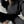 Vrouw in zwarte hoodie en joggingbroek, zittend op witte bank, draagt zilveren sneakers. Comfortabele loungewear, casual mode, streetwear stijl.