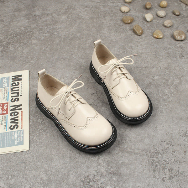 Beige leren veterschoenen voor kinderen op grijze vloer, naast stenen en krant. Stijlvolle kinderschoenen, casual en comfortabel ontwerp.