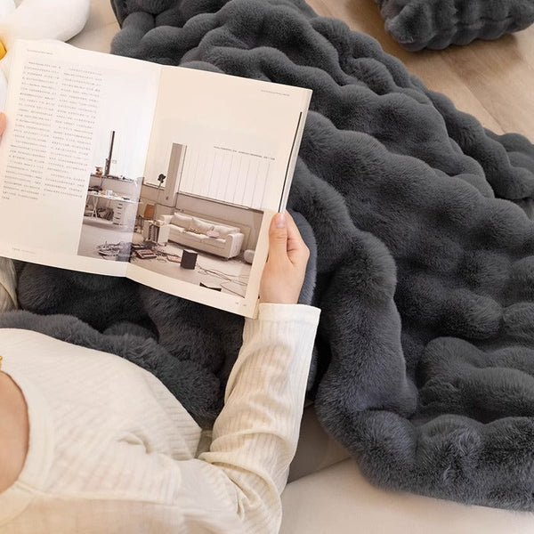 Persoon leest tijdschrift op grijze, pluizige deken; interieurinspiratie, comfortabele woonaccessoires, moderne woonkamer, ontspanning thuis.
