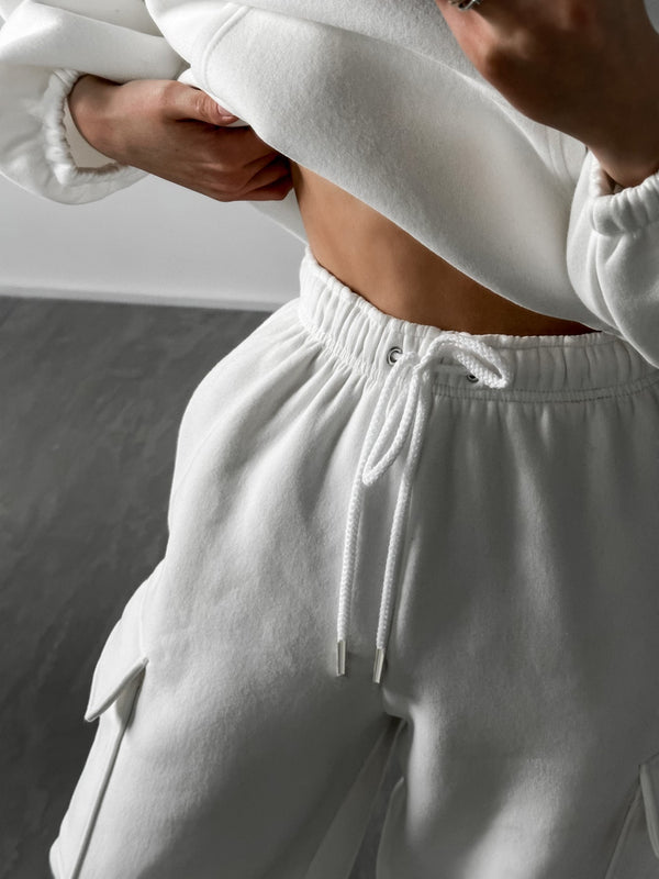 Vrouw in witte joggingbroek en trui toont blote buik. Comfortabele loungewear, casual mode, sportieve kledingstijl.