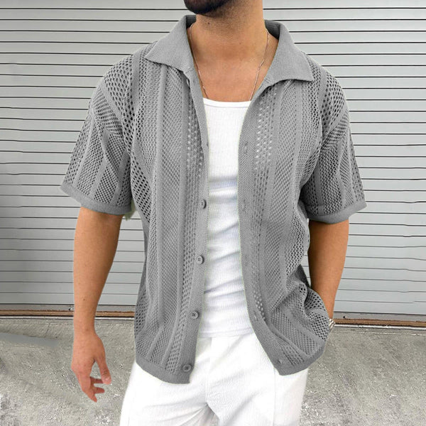 Grijze gebreide herenshirt met korte mouwen, opengewerkt patroon, gedragen over een wit hemd. Stijlvolle casual mode voor mannen.