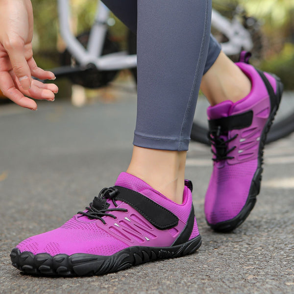 Paarse sportschoenen met zwarte veters en klittenband, gedragen door persoon op asfaltweg, fiets op achtergrond. Geschikt voor hardlopen en outdoor activiteiten.