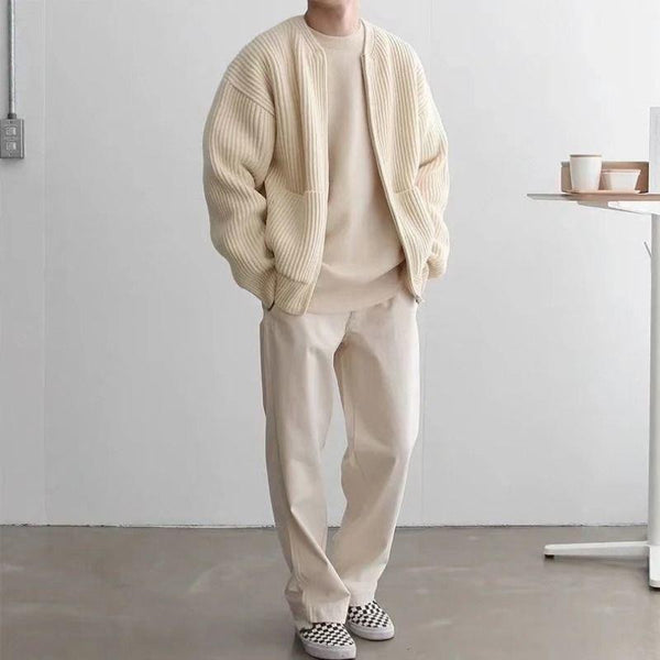 Man in crèmekleurige outfit met geribbelde jas, beige trui en broek, draagt zwart-wit geblokte schoenen. Moderne minimalistische mode.