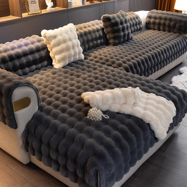 Donkergrijze, gewatteerde bankhoes met textuur, inclusief bijpassende kussens en witte accenten, in moderne woonkamer. Luxe interieurdecoratie.