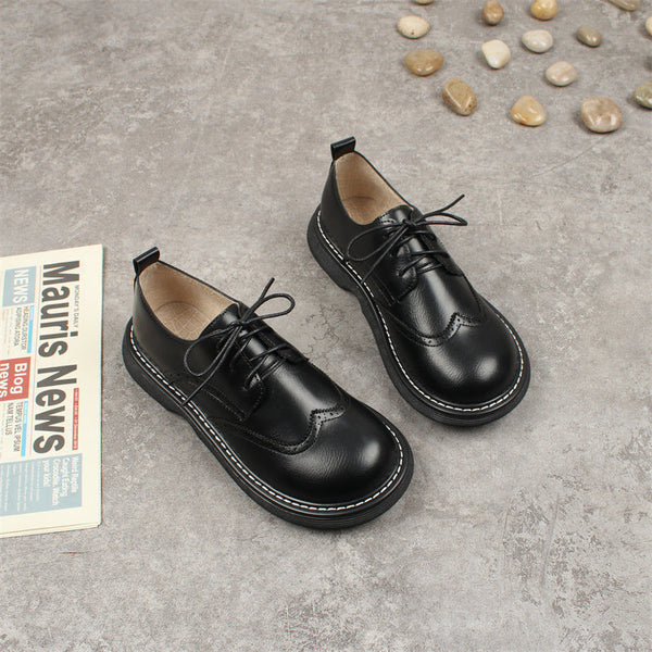 Zwarte leren kinderschoenen met veters op grijze vloer, naast krant en stenen. Stijlvolle en duurzame schoenen voor dagelijks gebruik.