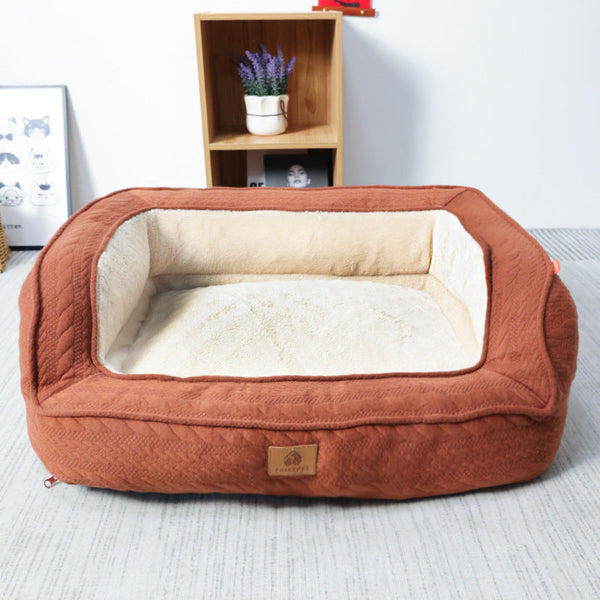 Bruin hondenbed met zachte, crèmekleurige binnenkant, geplaatst op een lichte vloer. Achtergrond bevat een houten plank met een plant en decoratie.