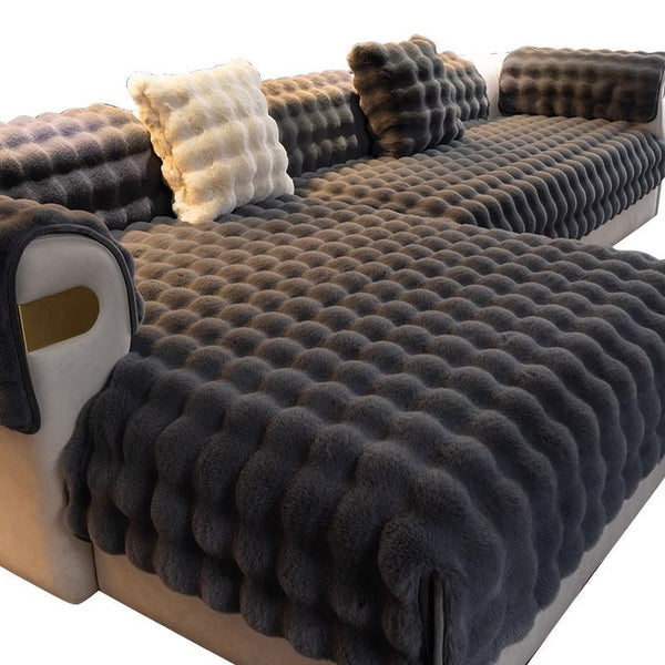 Grijze pluche bankhoes met gewatteerd patroon, inclusief bijpassende kussens en armleuningbeschermers, perfect voor moderne woonkamerinrichting.