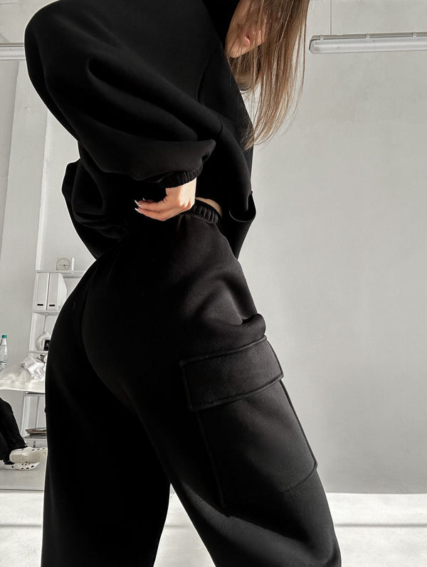 Vrouw in zwarte oversized sweater en cargobroek poseert in minimalistische studio. Modetrend, comfortabele kleding, streetwear stijl.