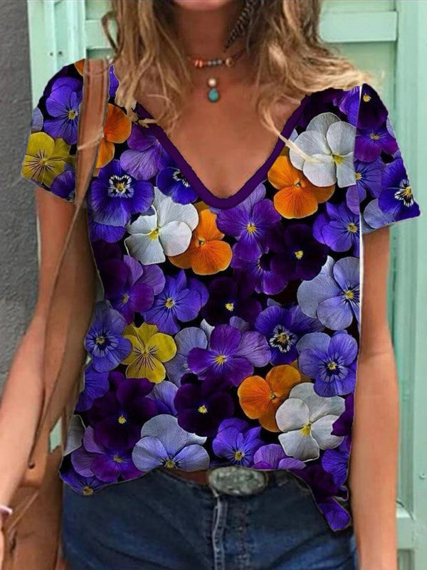 Vrouw draagt kleurrijk bloemen T-shirt met viooltjesprint, casual zomermode, trendy dameskleding, paarse en oranje bloemen, boho-stijl.