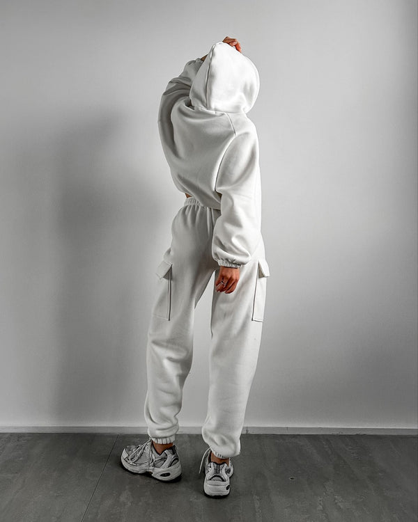 Vrouw in witte hoodie en joggingbroek, casual sportkleding, comfortabele mode, grijze sneakers, minimalistische achtergrond, streetwear stijl.